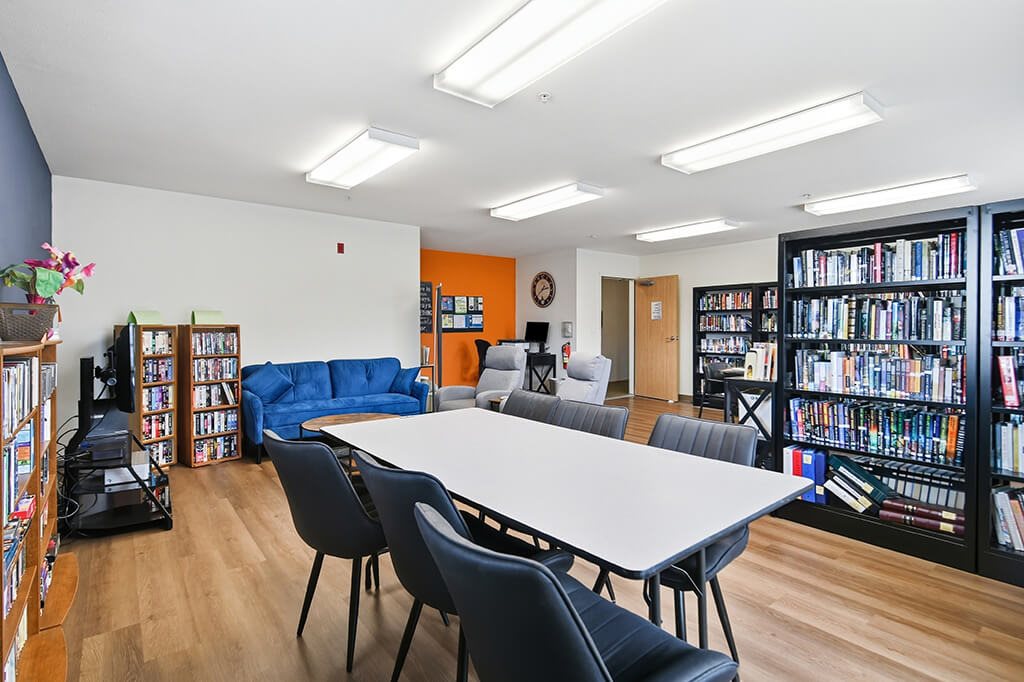 A library with a white table surrounded by chairs and bookshelves filled with books.